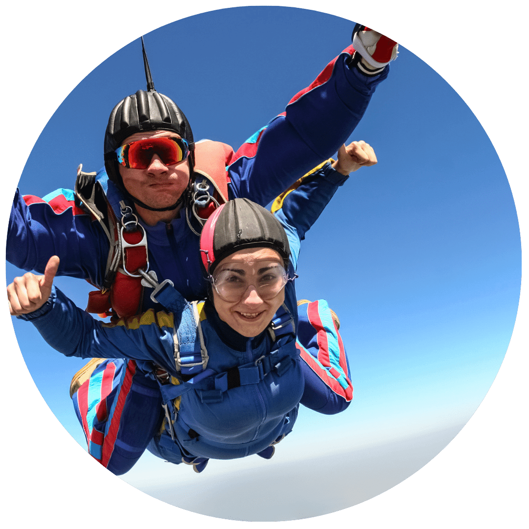 happy woman doing tandem skydiving with skydiving instructor wearing red goggles behind her